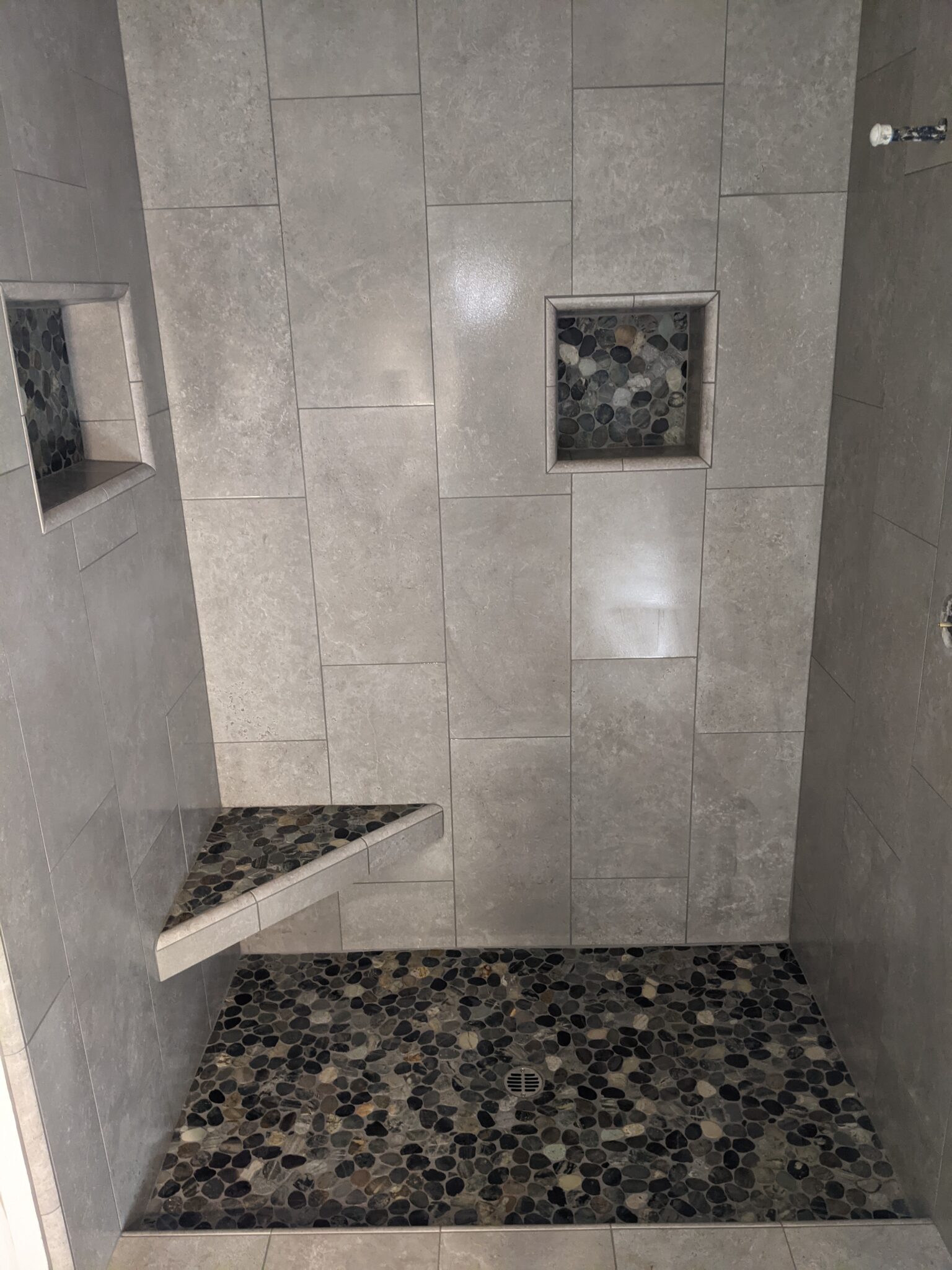 Shower with offset pattern on walls, pebble floor and corner seat with two niches