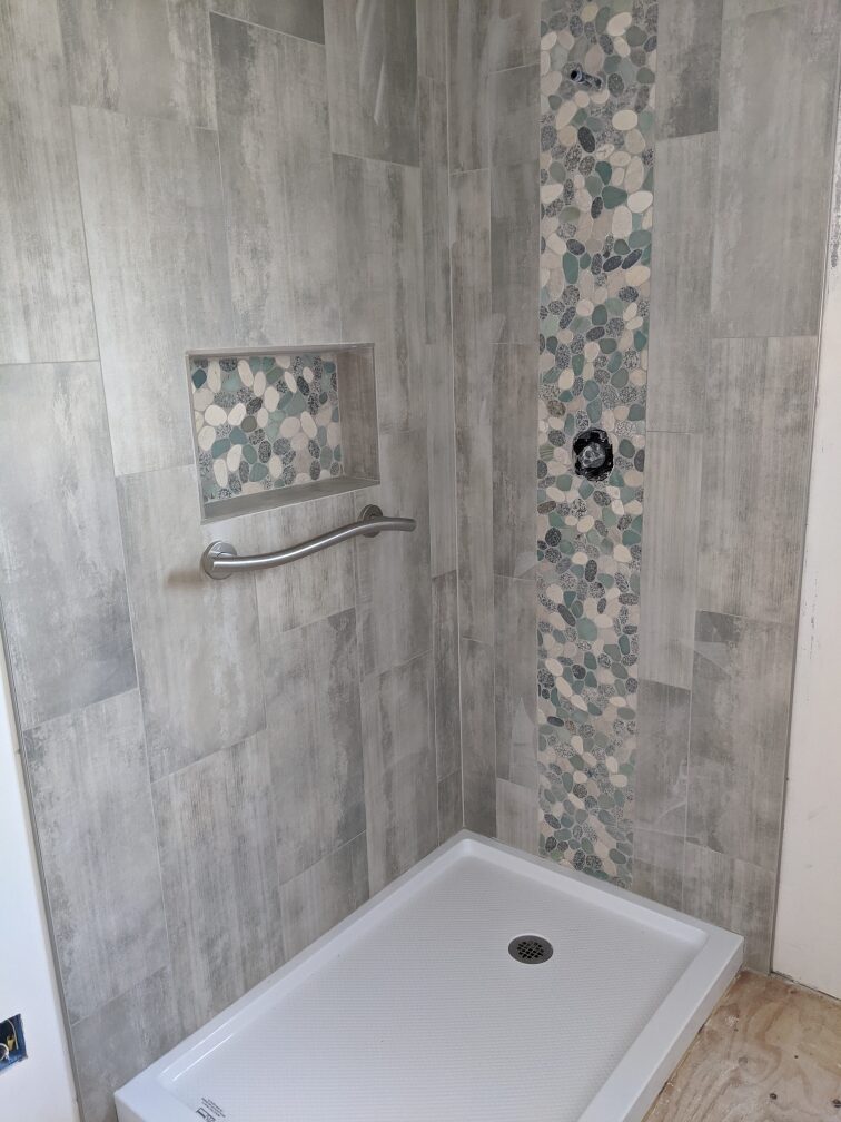 Tile shower with fiberglass pan and pebble installed on valve wall